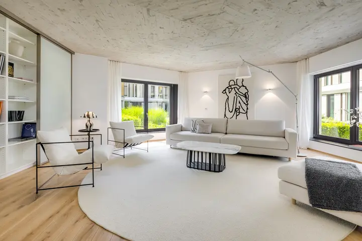 Wohnzimmer mit Sichtbetondecke, rundem Teppich und Sofa, Home Staging Architektur