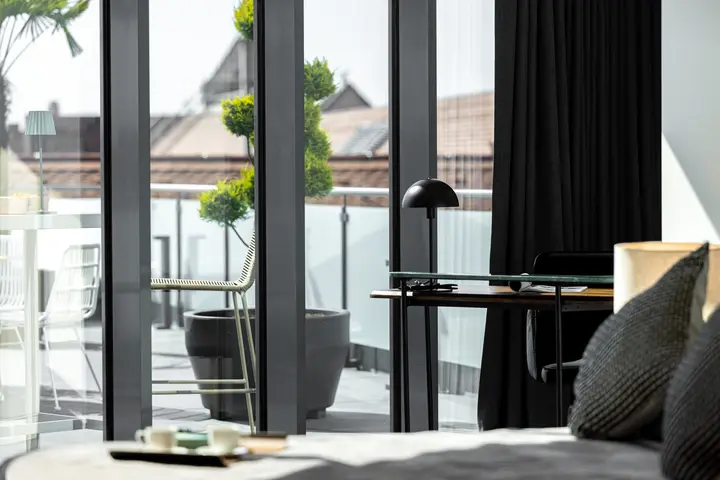 Bett vor bodentiefen Fenstern mit Formschnittbaum auf der Terrasse