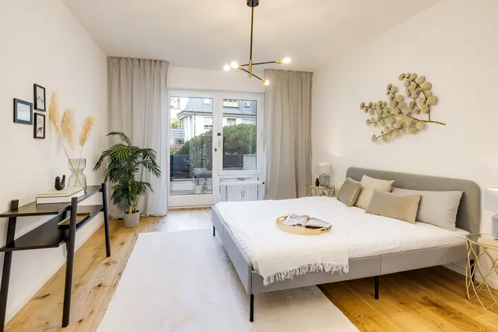 Schlafzimmer mit Doppelbett und Schreibtisch vor der Balkontür