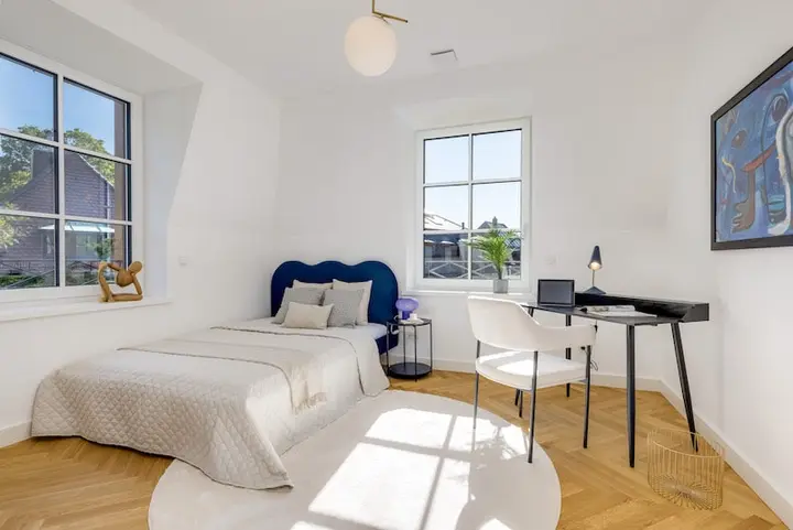 Schlaf- und Arbeitszimmer mit Bett und Schreibtisch unter Sprossenfenstern
