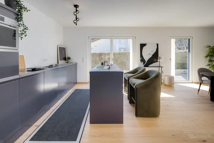 Küche mit dunkler Küchenzeile, Kochinsel und Sesseln in einem Neubau