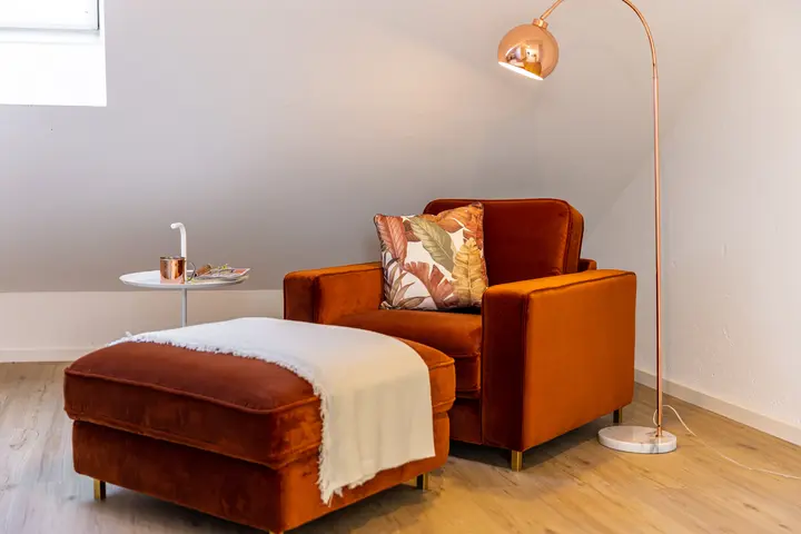 Orangefarbener Sessel mit Hocker und Bogenleuchte