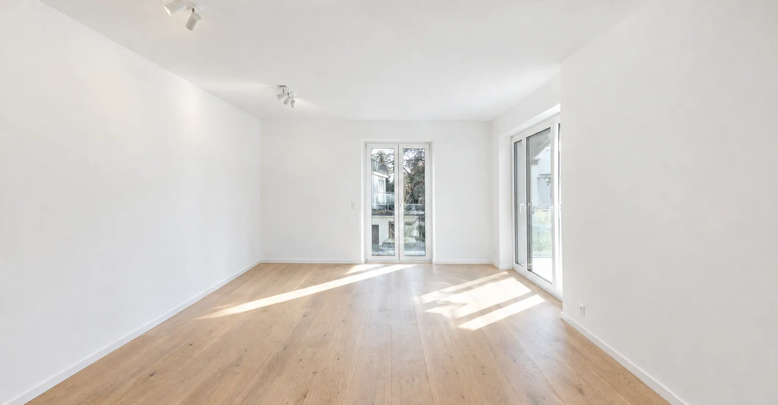 Leerer Raum mit zwei Balkontüren und Eichendielen vor dem Home Staging