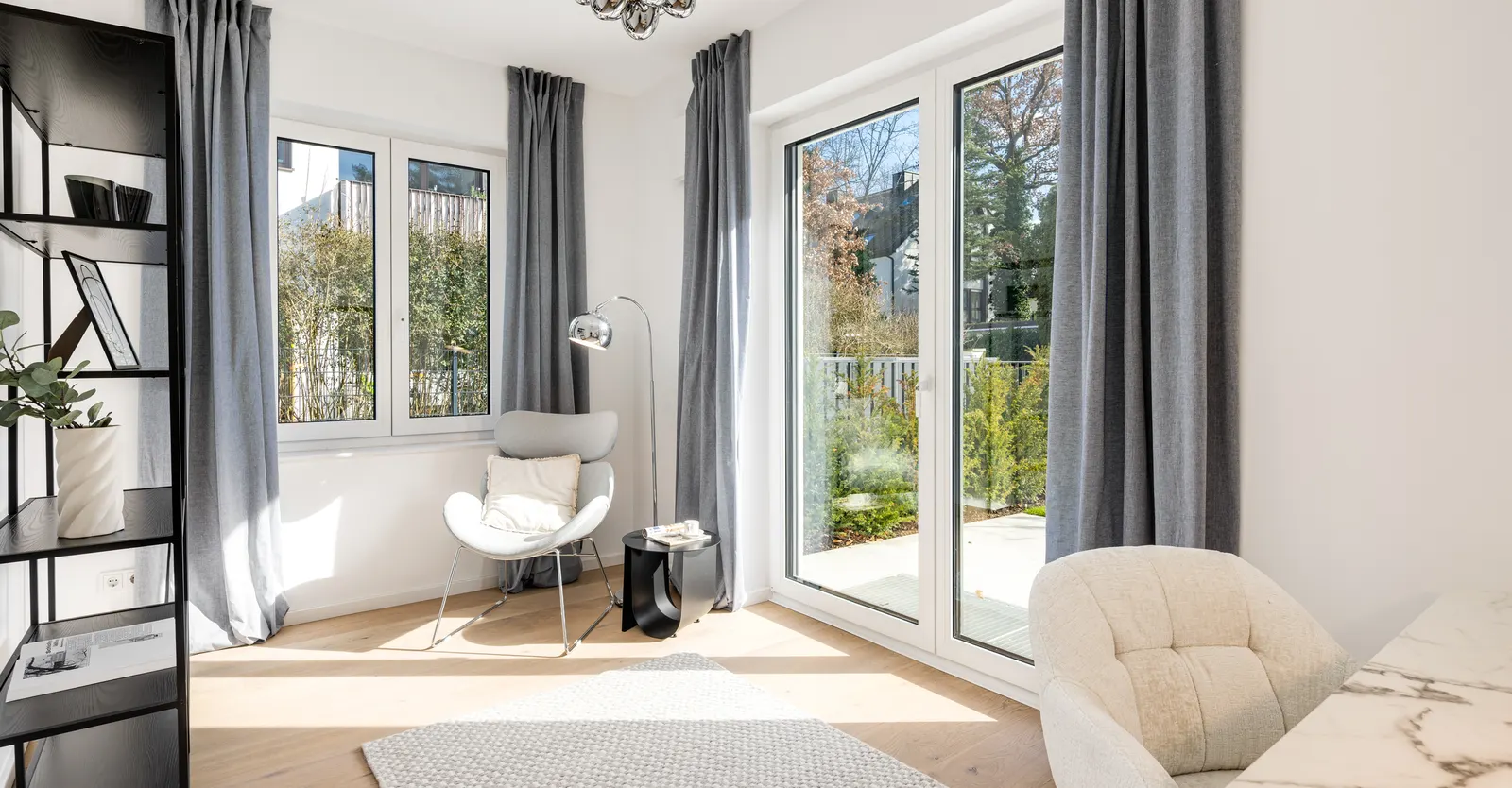 Wohnraum mit Sessel, Regal und Vorhängen an der Terrassentür