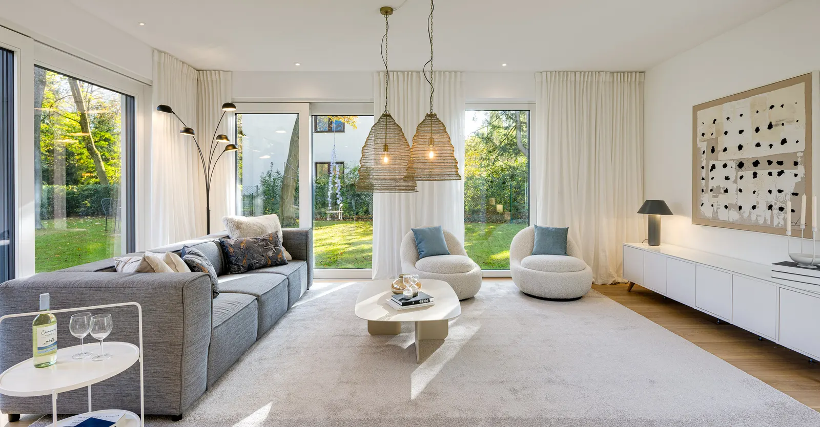 Wohnzimmer mit Ecksofa, Sesseln und Pendelleuchten vor bodentiefen Fenstern